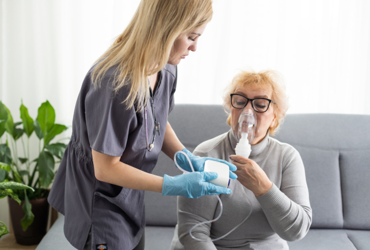 Young girl doctor makes inhalation to an older woman on a white background. Fights chronic respiratory conditions at home.