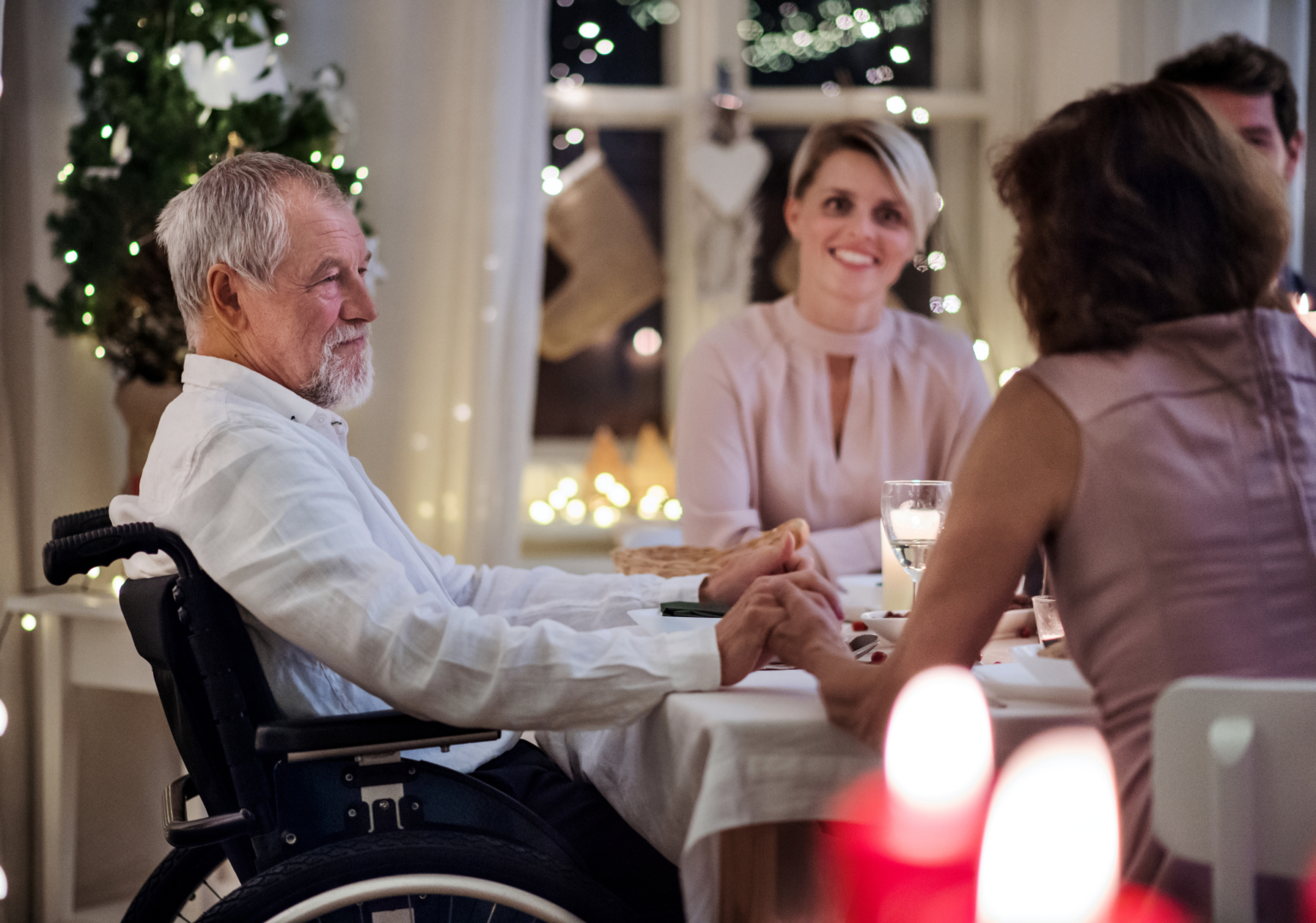 Happy senior man in wheelchair with family indoors celebrating Christmas together.